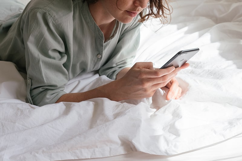 eine Frau, die ein Smartphone benutzt, während sie im Bett liegt