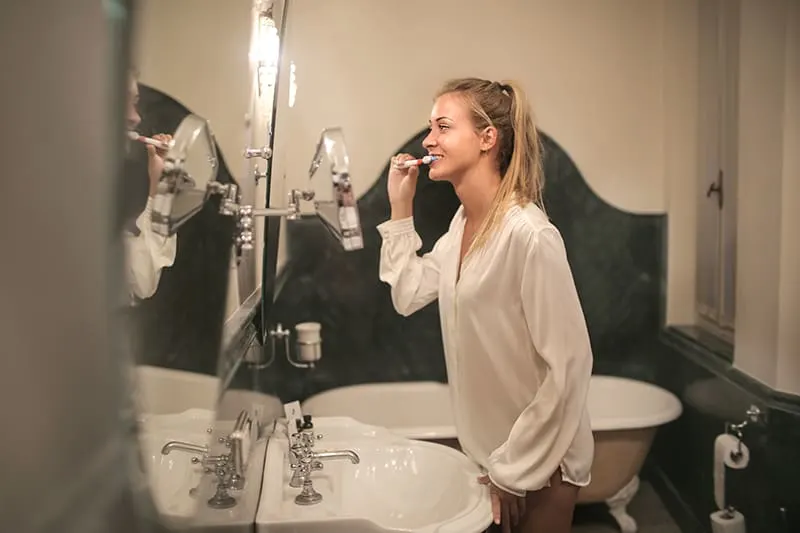 Eine Frau putzt sich die Zähne, während sie im Badezimmer vor dem Spiegel steht
