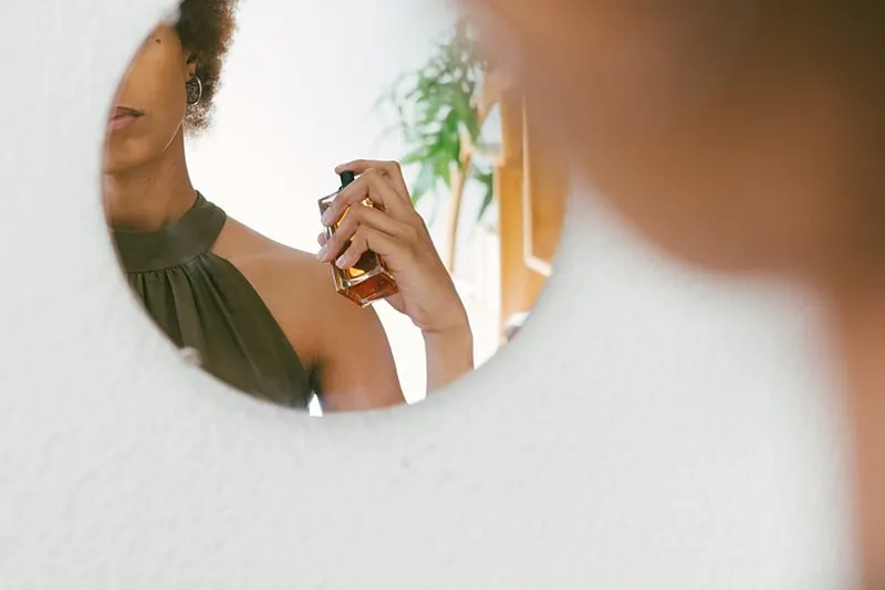 Eine Frau sprüht Parfüm auf ihren Körper, während sie vor dem Spiegel steht