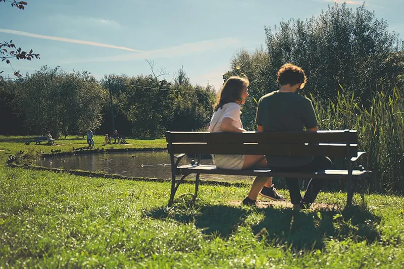 Eine Frau und ein Mann sitzen während des Dates auf der Bank in der Nähe des Sees im Park