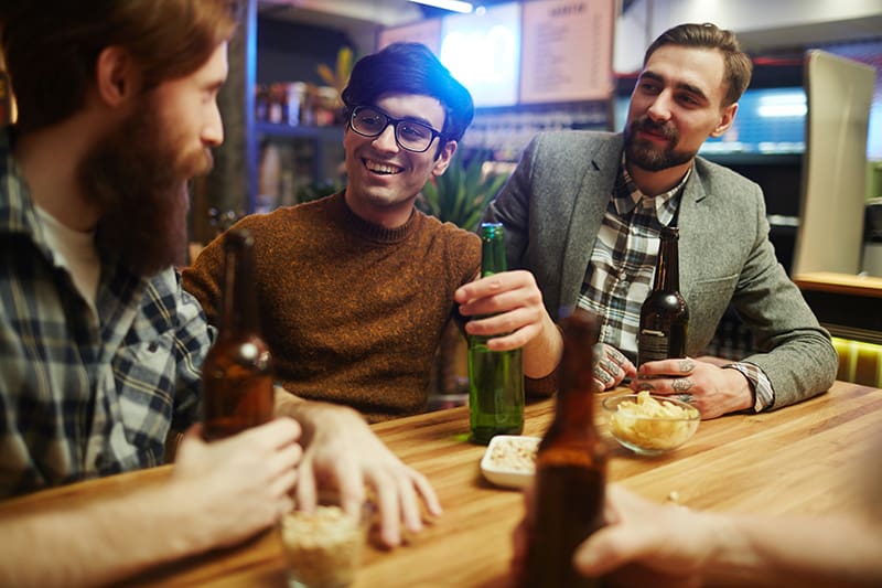 eine Gruppe männlicher Freunde, die lächeln und reden, während sie in der Bar trinken