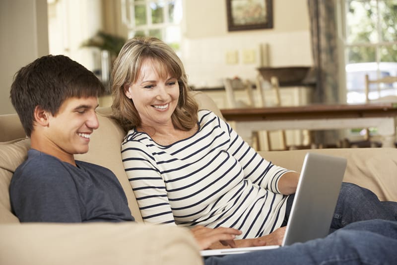 Eine Mutter und ein Sohn betrachten den Laptop, während sie zu Hause auf dem Sofa sitzen
