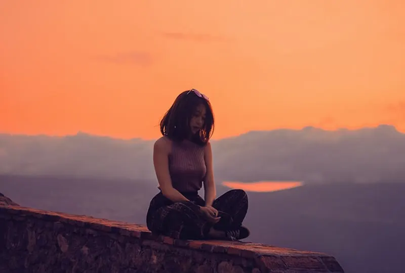 eine einsame Frau, die während des Sonnenuntergangs auf der Betonwand sitzt