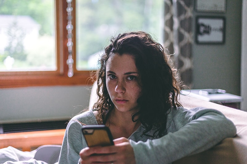 eine ernste Frau, die ein Smartphone hält, während sie auf der Couch sitzt