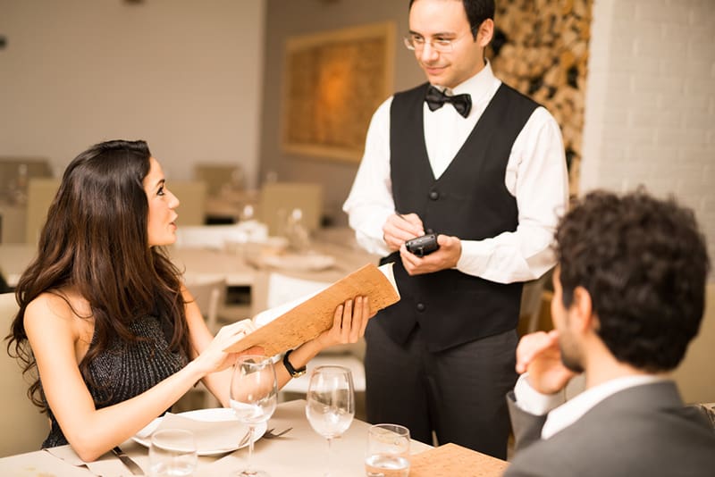eine höfliche Frau, die bei einem Kellner bestellt, während sie mit einem Mann am Tisch sitzt