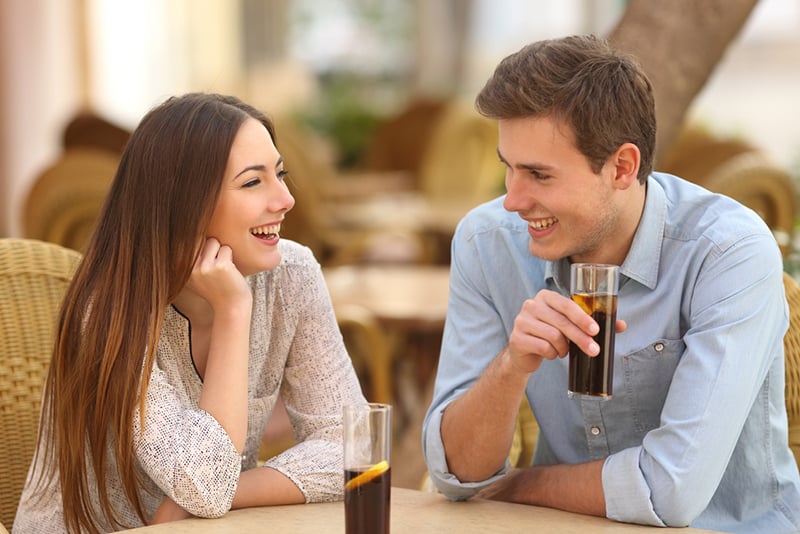 eine lächelnde Frau, die einem Mann zuhört, der mit ihr spricht, während er zusammen im Café sitzt