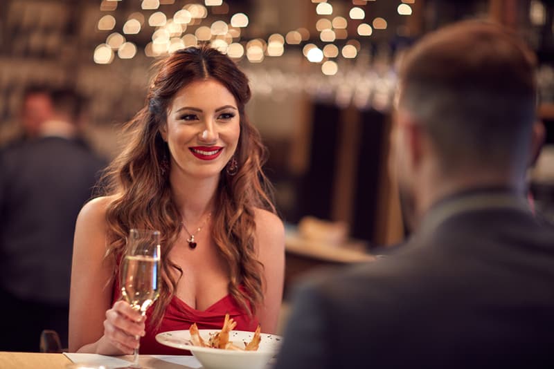 eine lächelnde selbstbewusste Frau, die mit einem Mann im Restaurant sitzt und ein Glas Champagner hält