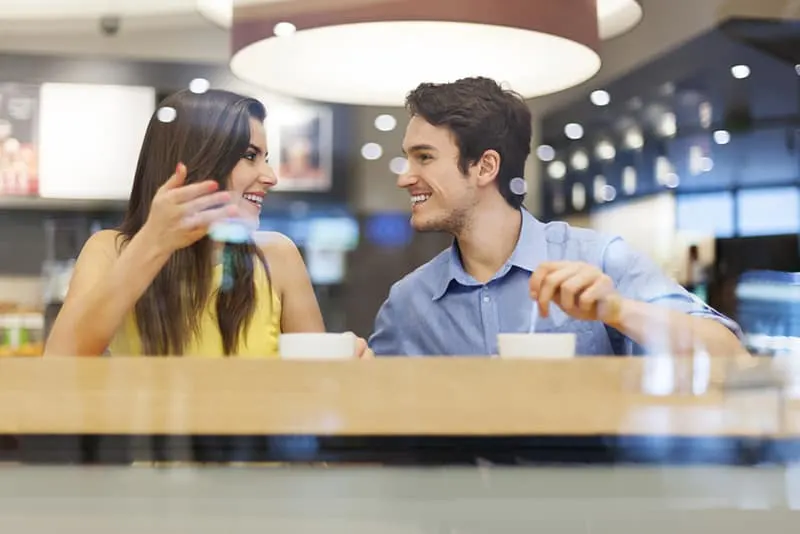eine lächelnde Frau, die mit einem lächelnden Mann im Café am Datum spricht