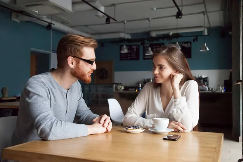 eine lächelnde Frau, die mit einem männlichen Freund flirtet, während sie zusammen im Café sitzt