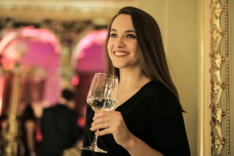 eine lächelnde Dame, die ein Glas Wein hält, während sie allein auf der Party steht