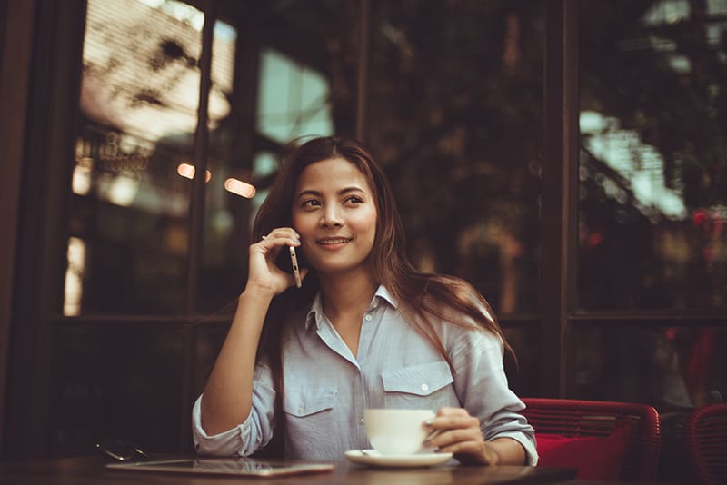 eine lächelnde Frau, die am Telefon spricht, während sie im Café sitzt