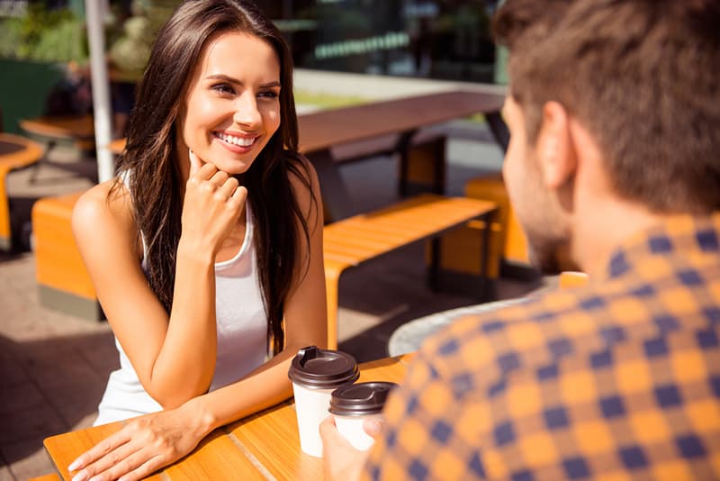 eine lächelnde Frau, die zu ihrem männlichen Freund schaut, während sie zusammen im Café sitzt