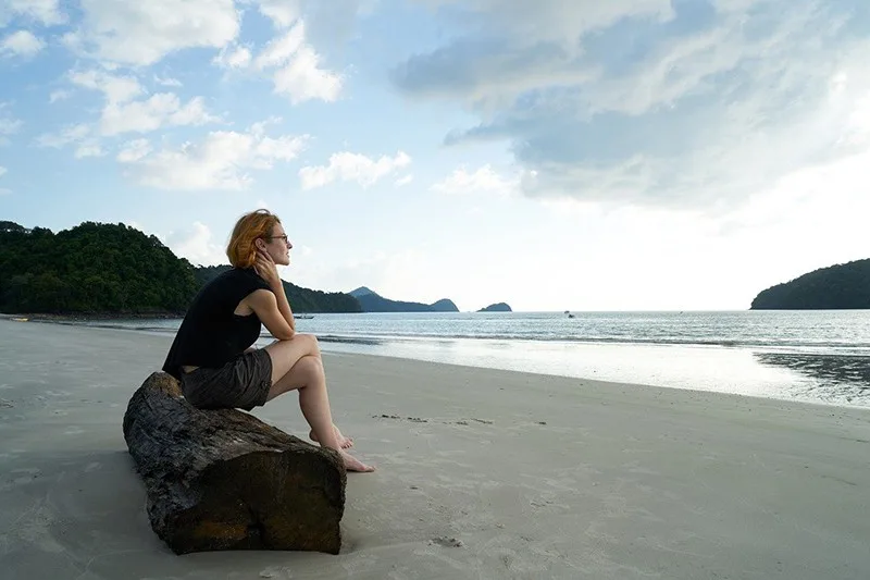 eine nachdenkliche Frau, die alleine am Strand sitzt und auf das Meer schaut