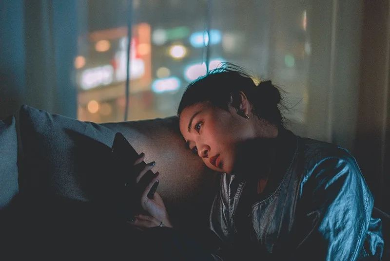 eine traurige Frau, die Smartphone betrachtet, während sie in der Nacht auf der Couch sitzt