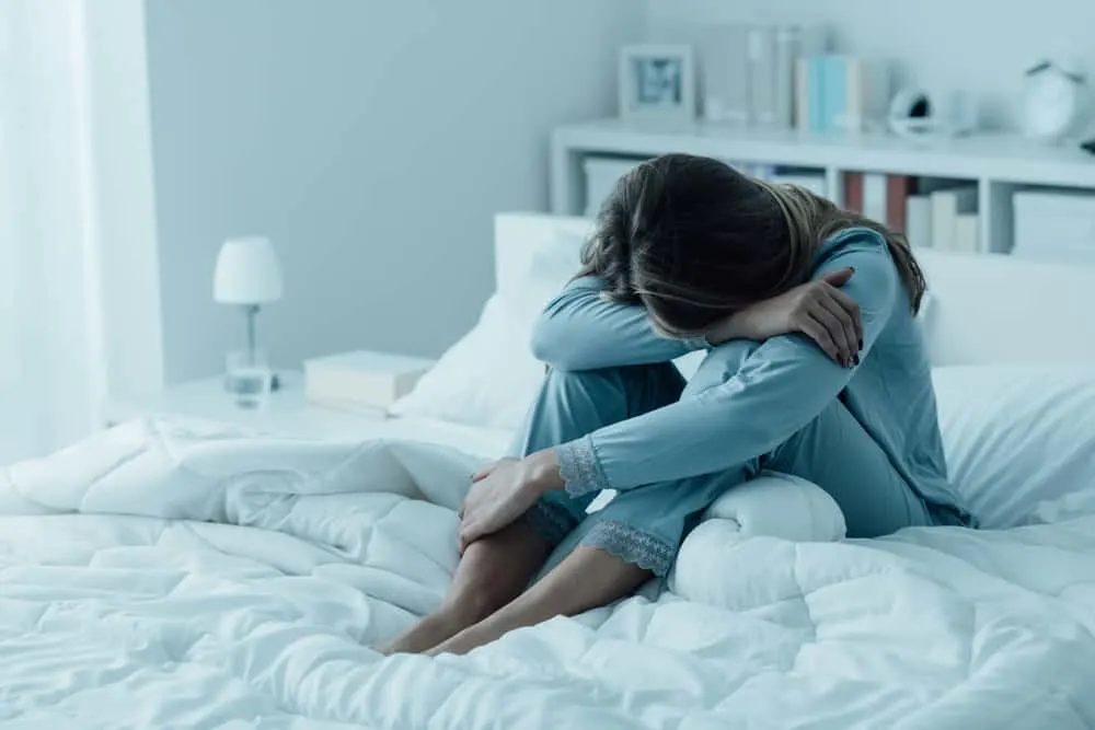 eine traurige Frau im Pyjama, die auf dem Bett sitzt