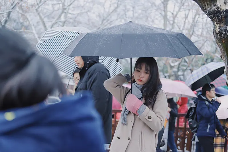 eine traurige Frau, die einen Regenschirm hält, während sie in der Menge steht