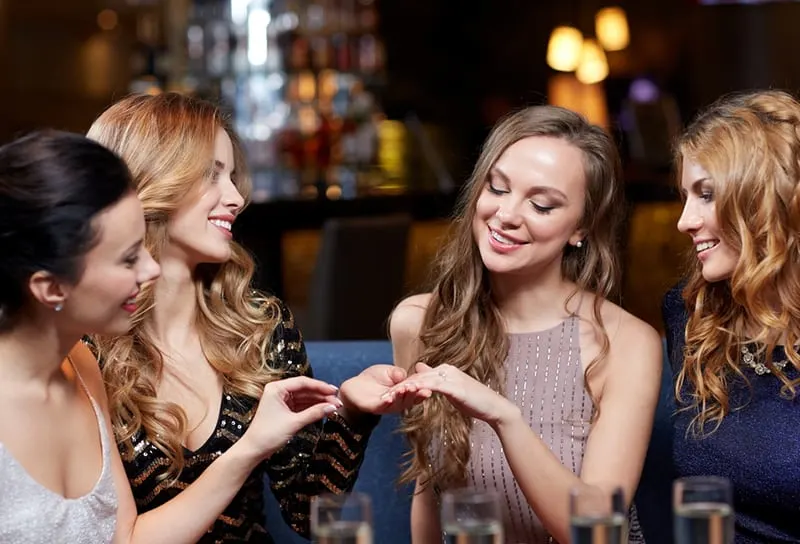 glückliche Frau, die ihren Freunden im Nachtclub Verlobungsring zeigt