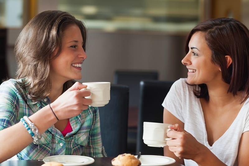 zwei lächelnde weibliche Bekanntschaft, die zusammen Kaffee im Café trinkt