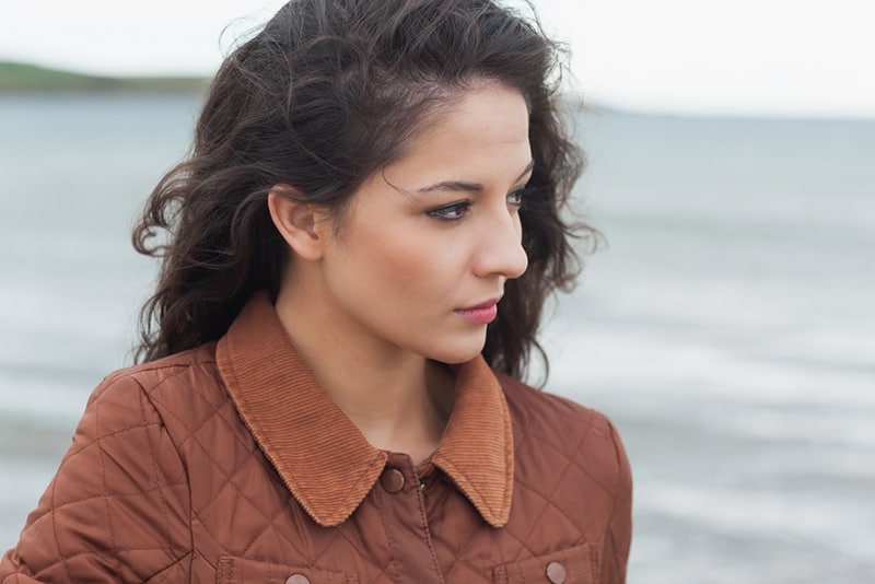 nachdenkliche junge Frau mit braunen Haaren, die am Strand stehen