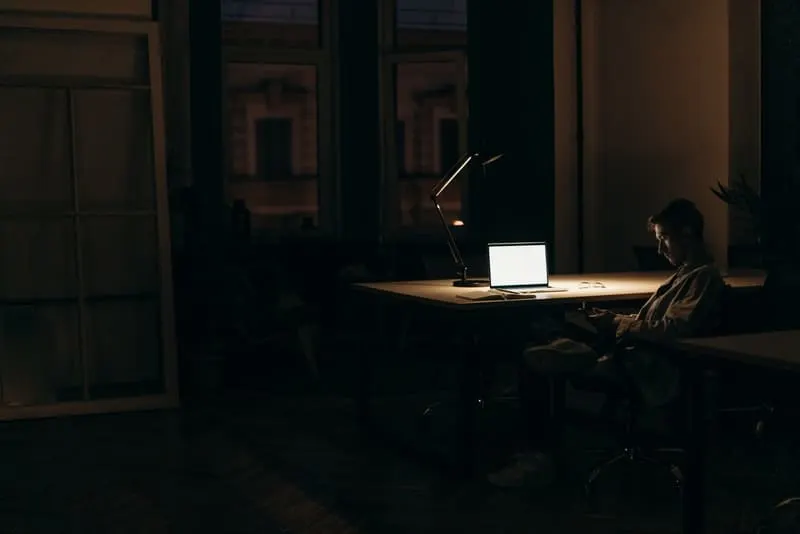 Abends sitzt ein Mann an einem Schreibtisch und benutzt ein Smartphone