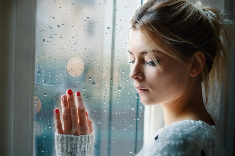 Ein trauriges Mädchen schaut an einem regnerischen Tag aus dem Fenster