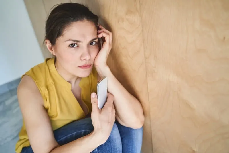 Eine enttäuschte Frau hockt mit einem Handy in der Hand