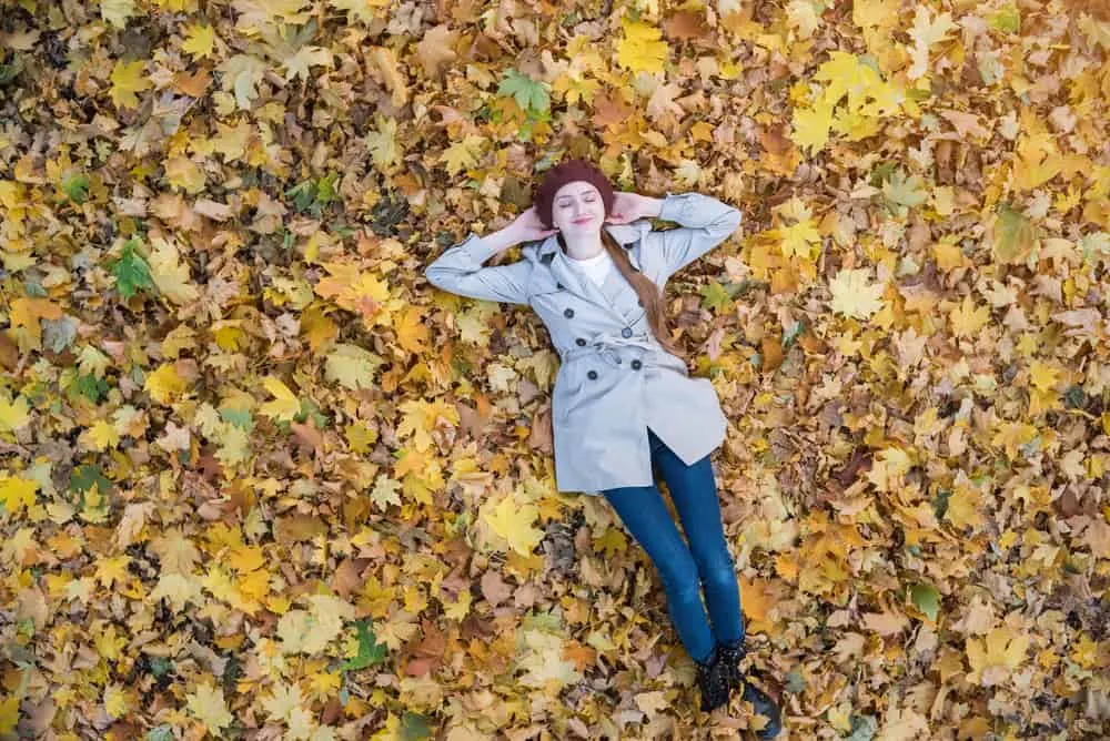 Auf den trockenen Blättern liegt eine junge lächelnde Frau in einem grauen Mantel
