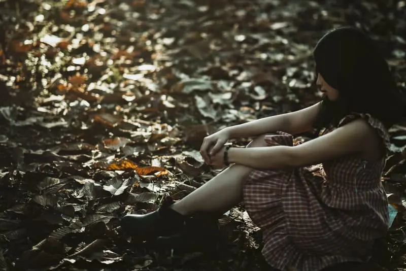 Auf einem trockenen Blatt im Wald sitzt eine traurige Frau in einem Kleid
