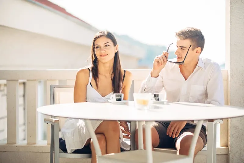 lächelnde nachdenkliche Frau, die beiseite schaut, während im Café mit einem Mann auf einem Datum sitzt