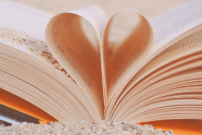 Buchblätter in Herzform gefaltet und Sand auf dem Buch
