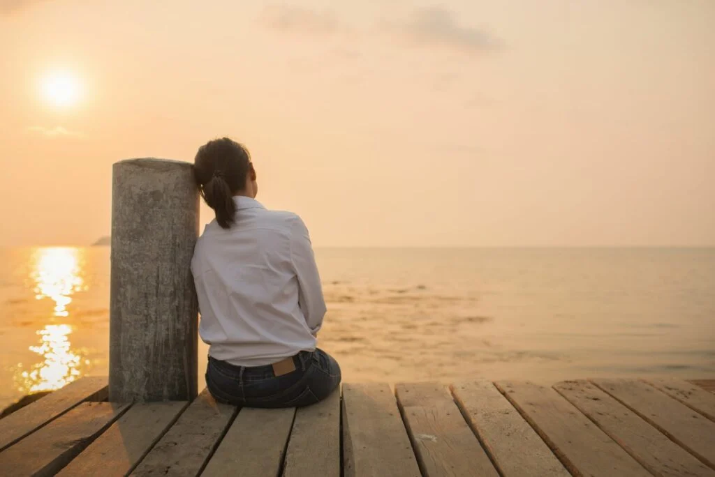 Das Maedchen sitzt auf dem Pier und blickt auf das Meer