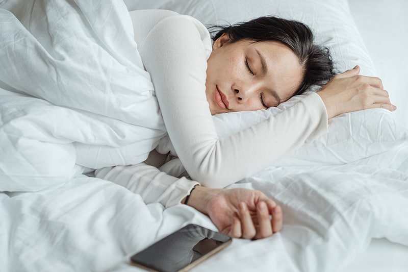 eine Frau, die in einem Bett mit weißen Laken schläft