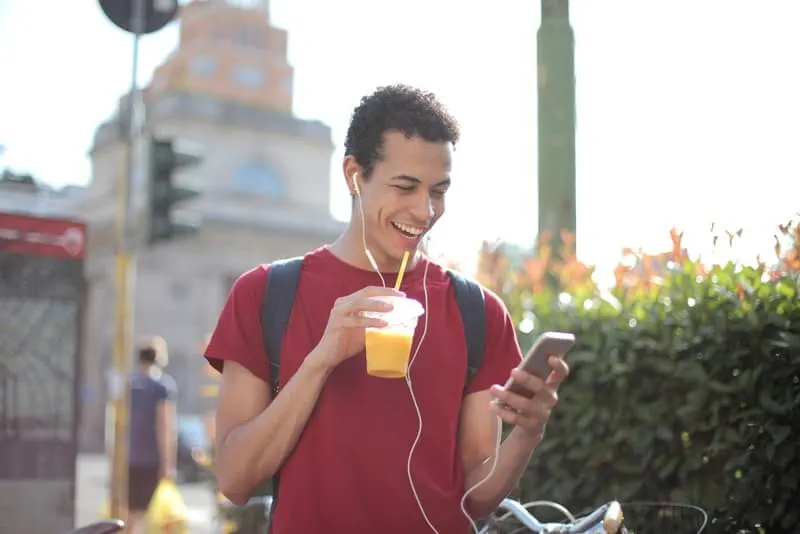 Draußen steht ein lächelnder Mann in einem roten T-Shirt und schaut sich etwas auf seinem Handy an