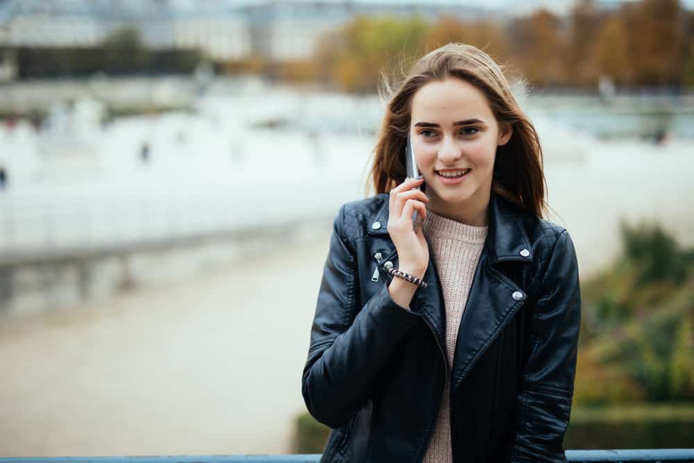 Draußen steht ein lächelndes Mädchen in einer Lederjacke und spricht auf ihrem Handy