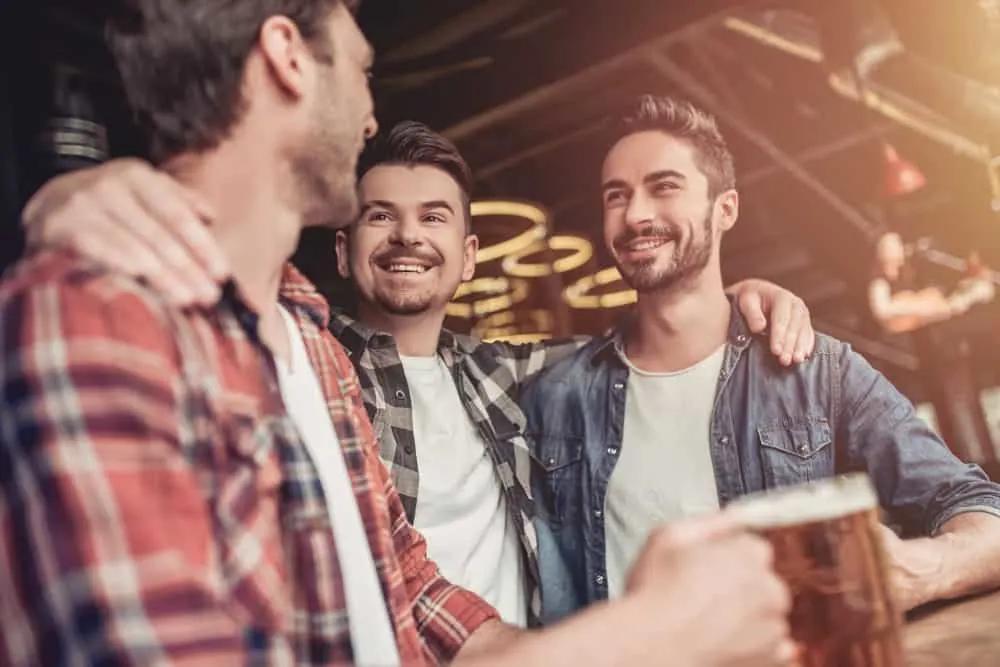 Drei lächelnde Männer trinken Bier an der Bar