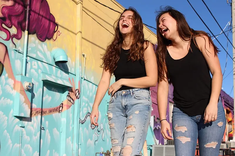 zwei lachende Mädchen, die nahe der Graffitiwand gehen
