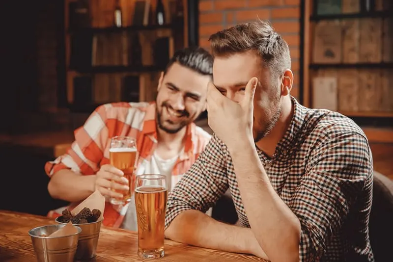 Ein Mann berührt seinen Kopf, während er mit einem Freund in einer Bar lacht