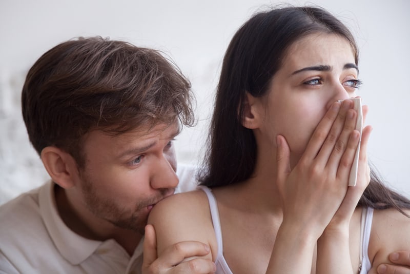 Ein Mann küsst die Schulter der Frau, während sie weint und Taschentücher auf der Nase hält