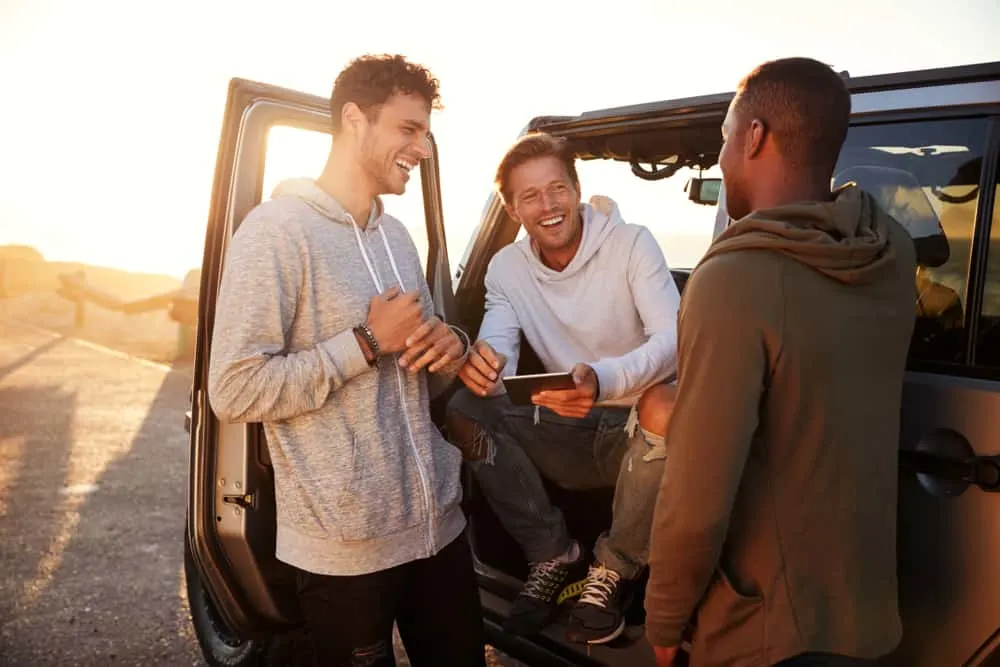 Ein Mann mit Freunden steht am Auto und lacht