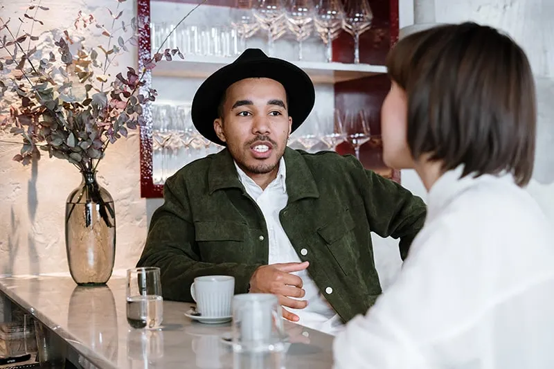 Ein Mann mit Hut spricht mit einer Frau bei einem Date im Café
