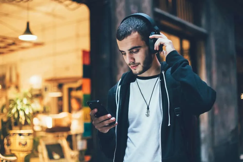 Ein Mann steht mit Kopfhörern draußen und benutzt ein Smartphone