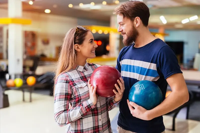 Ein Mann und eine Frau halten Bowlingkugeln, während sie lächeln und sich ansehen