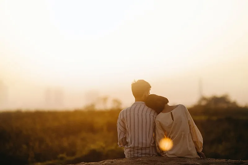 Ein Mann und eine Frau sitzen auf dem Boden und stützen sich aufeinander, während sie den Sonnenuntergang beobachten