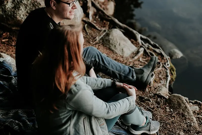 Ein Mann und eine Frau unterhalten sich neben dem Fluss und sitzen auf dem Boden