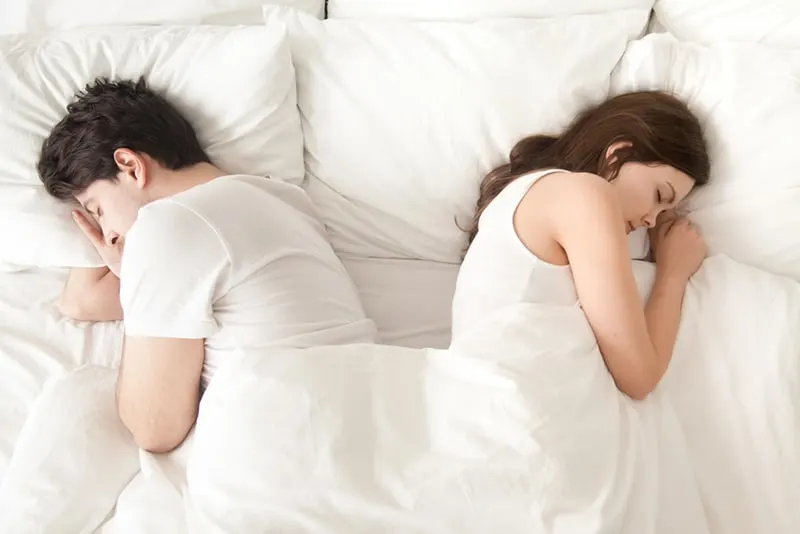 Ein gleichgültiger Mann und eine gleichgültige Frau, die getrennt hintereinander im Bett schlafen und Beziehungsprobleme haben