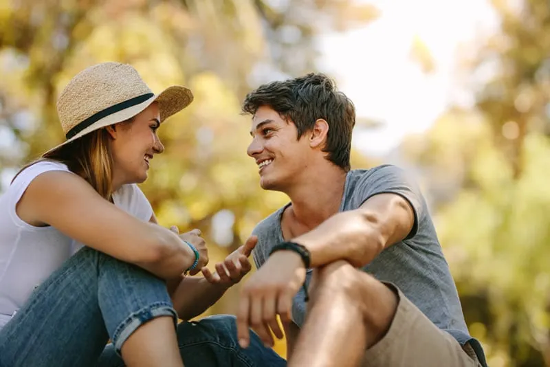 Ein lächelnder Mann und eine Frau sprechen miteinander, während sie im Park sitzen