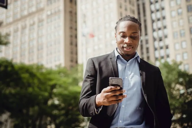 Ein lächelnder schwarzer Mann steht draußen und benutzt ein Smartphone