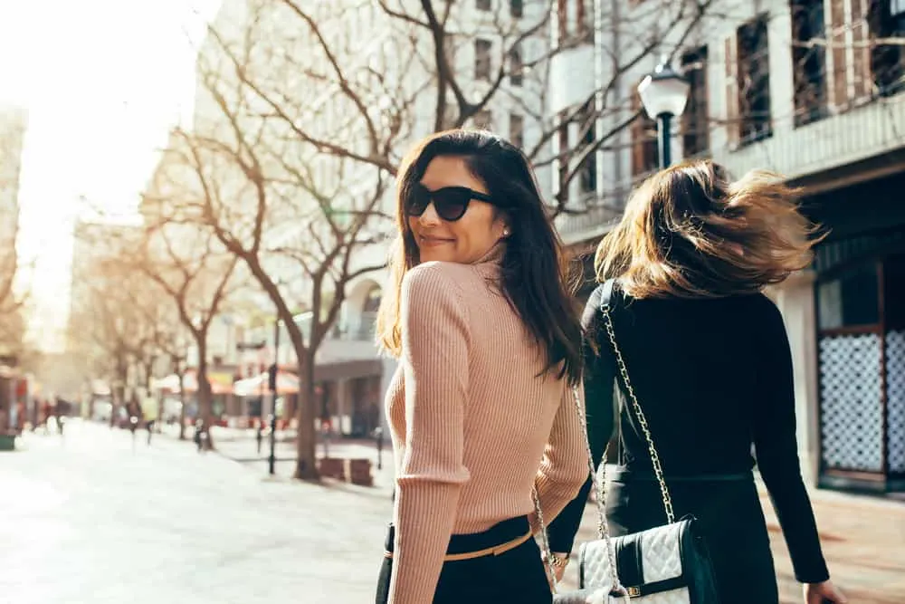 Ein lächelndes Mädchen mit Sonnenbrille geht mit einem Freund die Straße entlang
