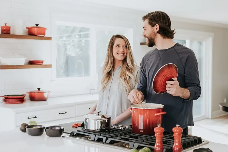 Ein lächelndes Paar, das sich beim gemeinsamen Zubereiten einer Mahlzeit in der Küche ansieht