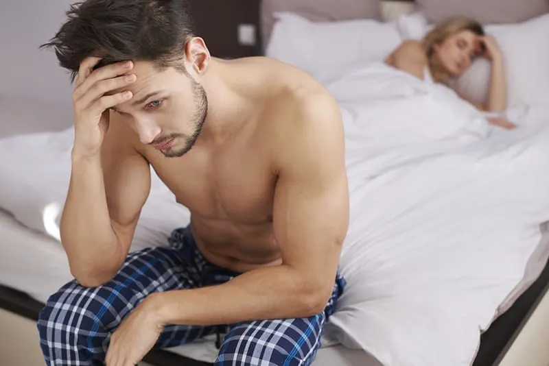 Ein nachdenklicher Mann sitzt auf dem Bett, während seine Freundin schläft